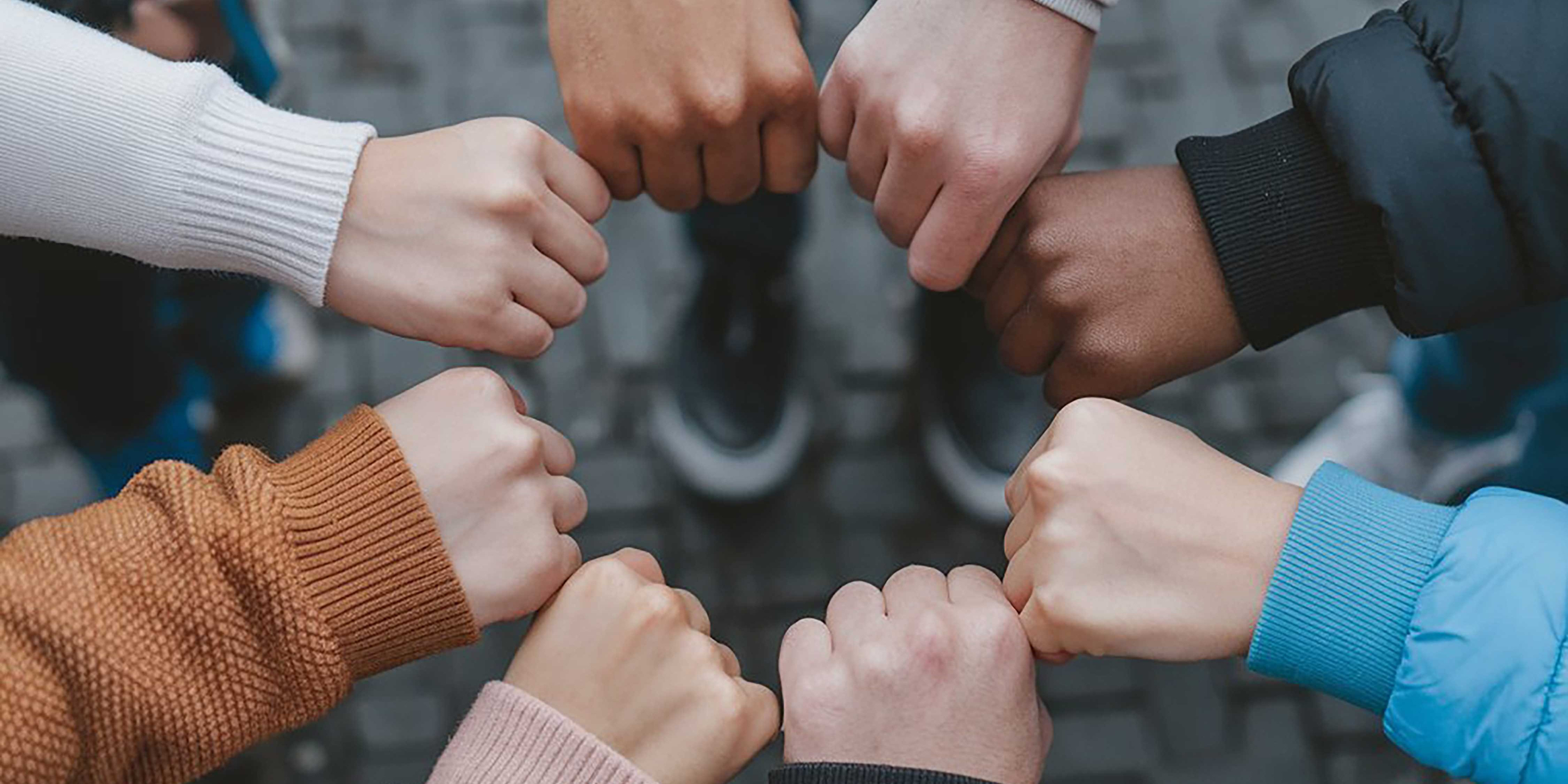 A circle of young people with their fists together to show unity.
