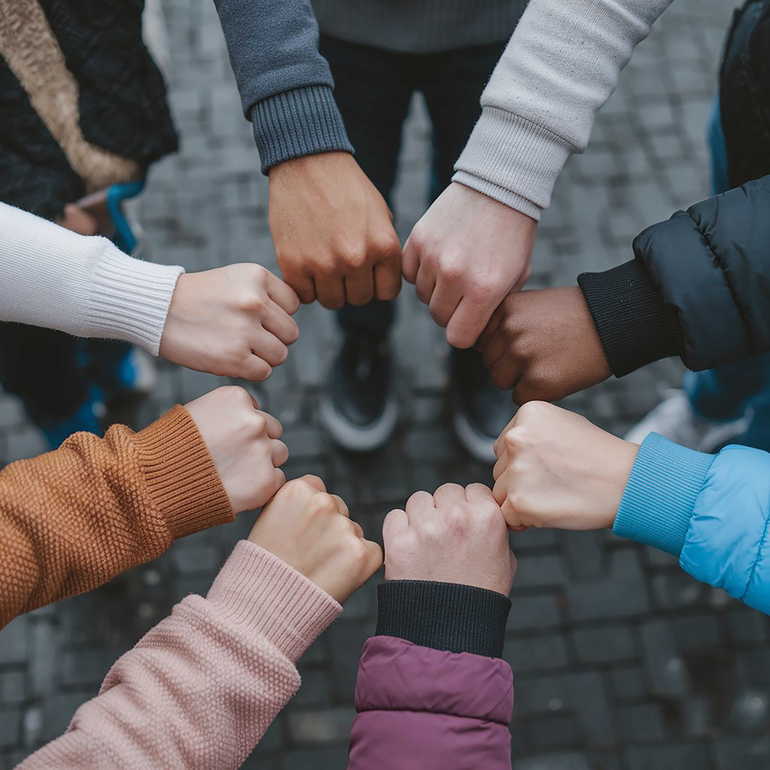 A circle of young people with their fists together to show unity.