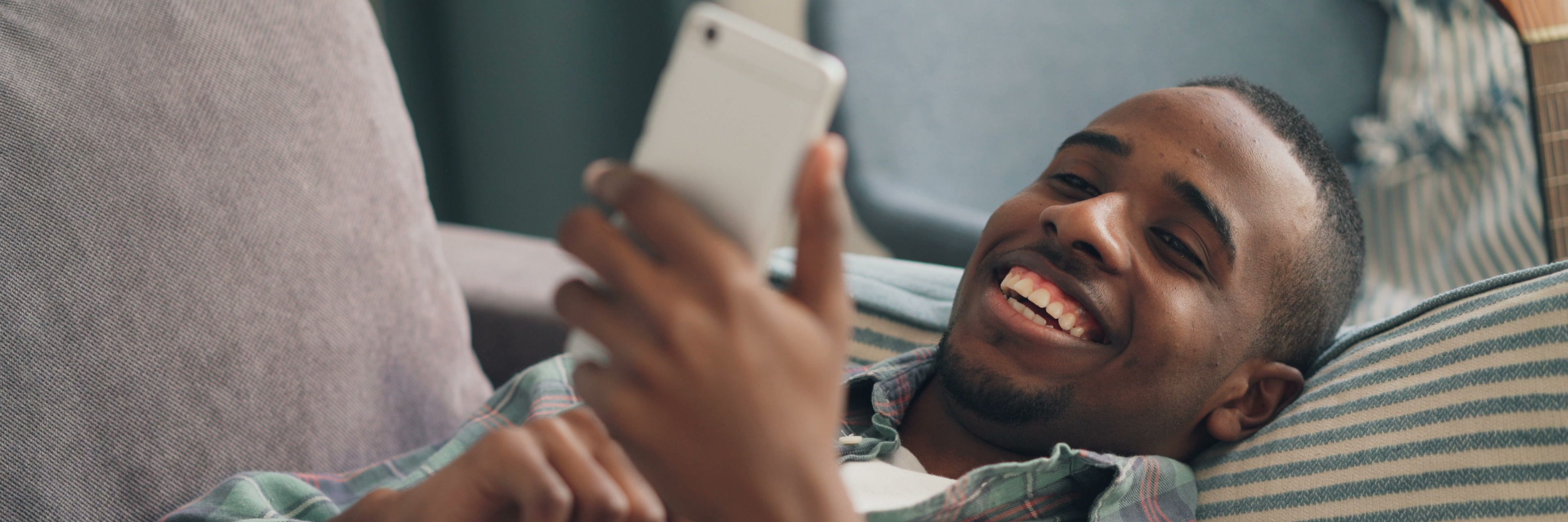 A man relaxing on a sofa, grinning at his phone.