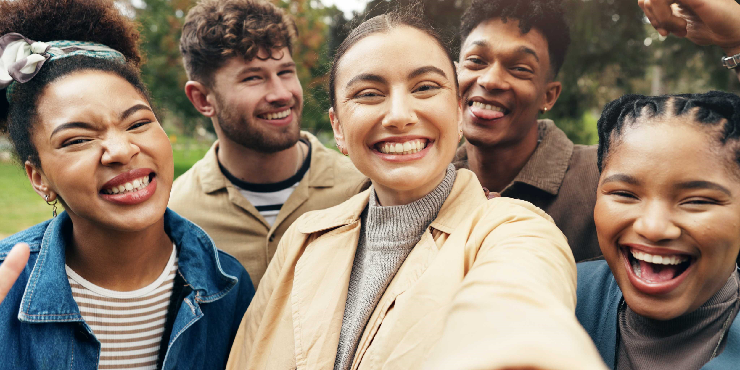 A diverse group of young people laughing and smiling in a park.