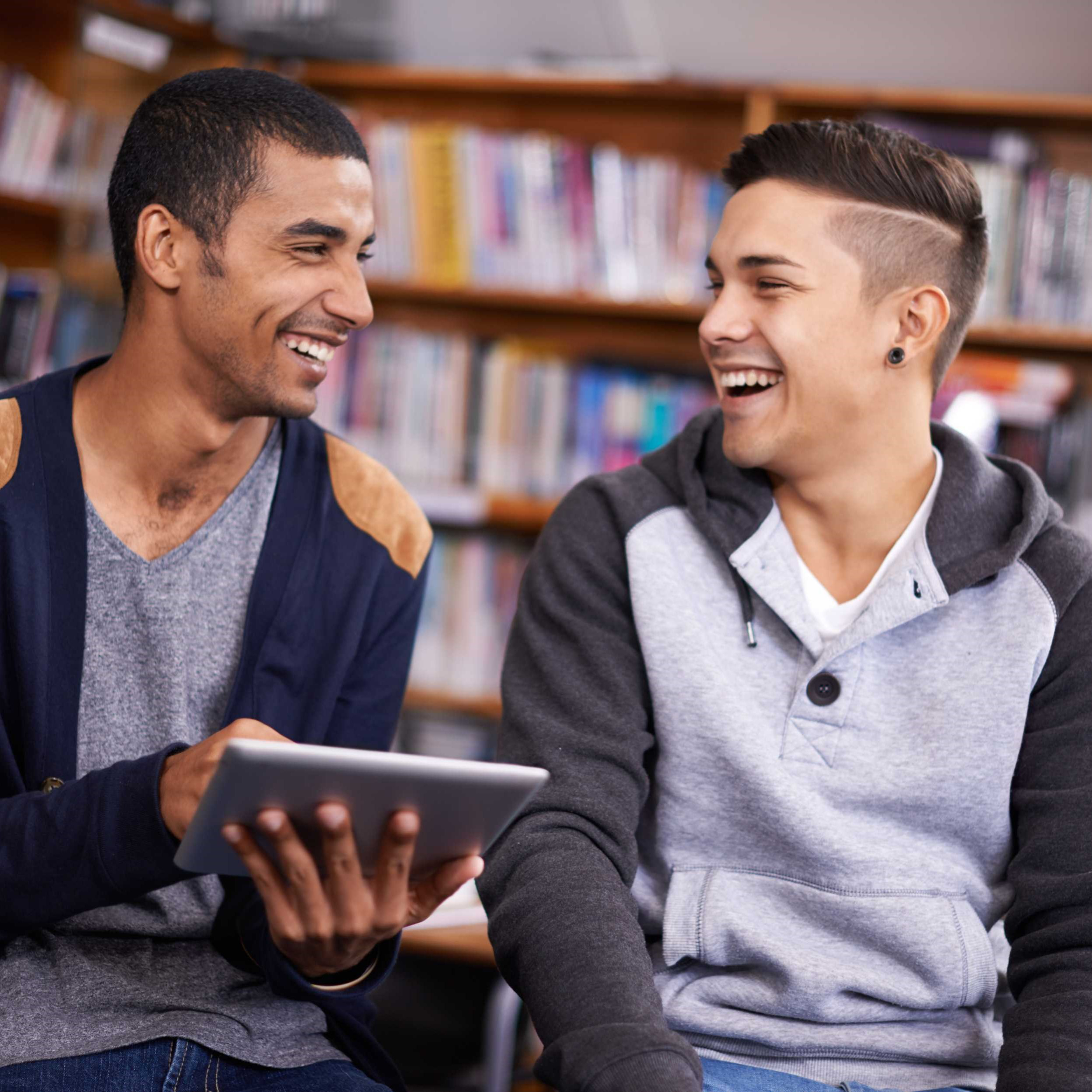 Two young men laughing together in a library.
