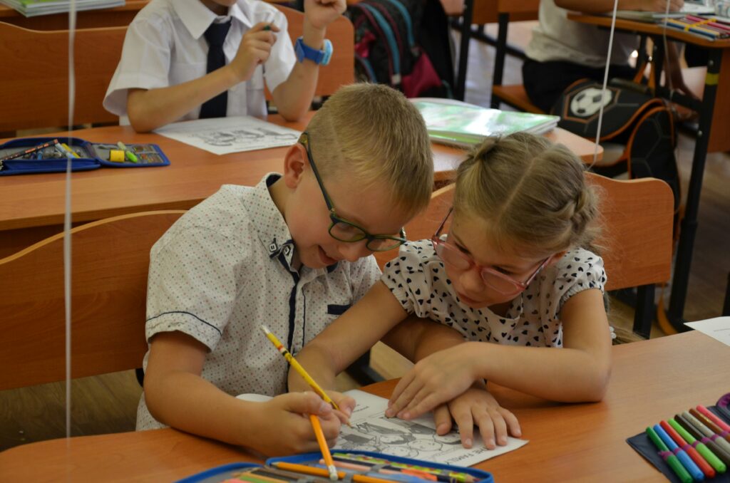 A young boy and young girl working together on a colouring-in sheet, in a classroom.