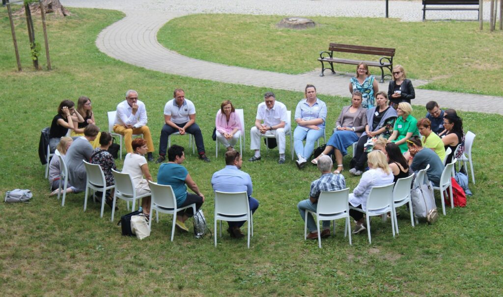 A large group of people seated in a circle, having a discussion in a park.