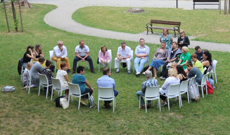 A large group of people seated in a circle, having a discussion in a park.