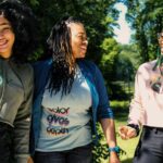 Three teenage girls laughing and smiling in a park.
