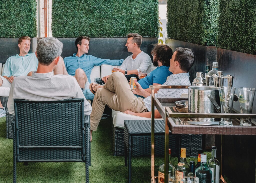 A group of men on a balcony, sitting around talking over drinks.