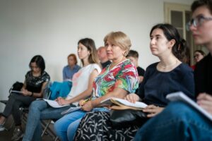 A diverse group of people attending a language class, seated rows and taking notes.